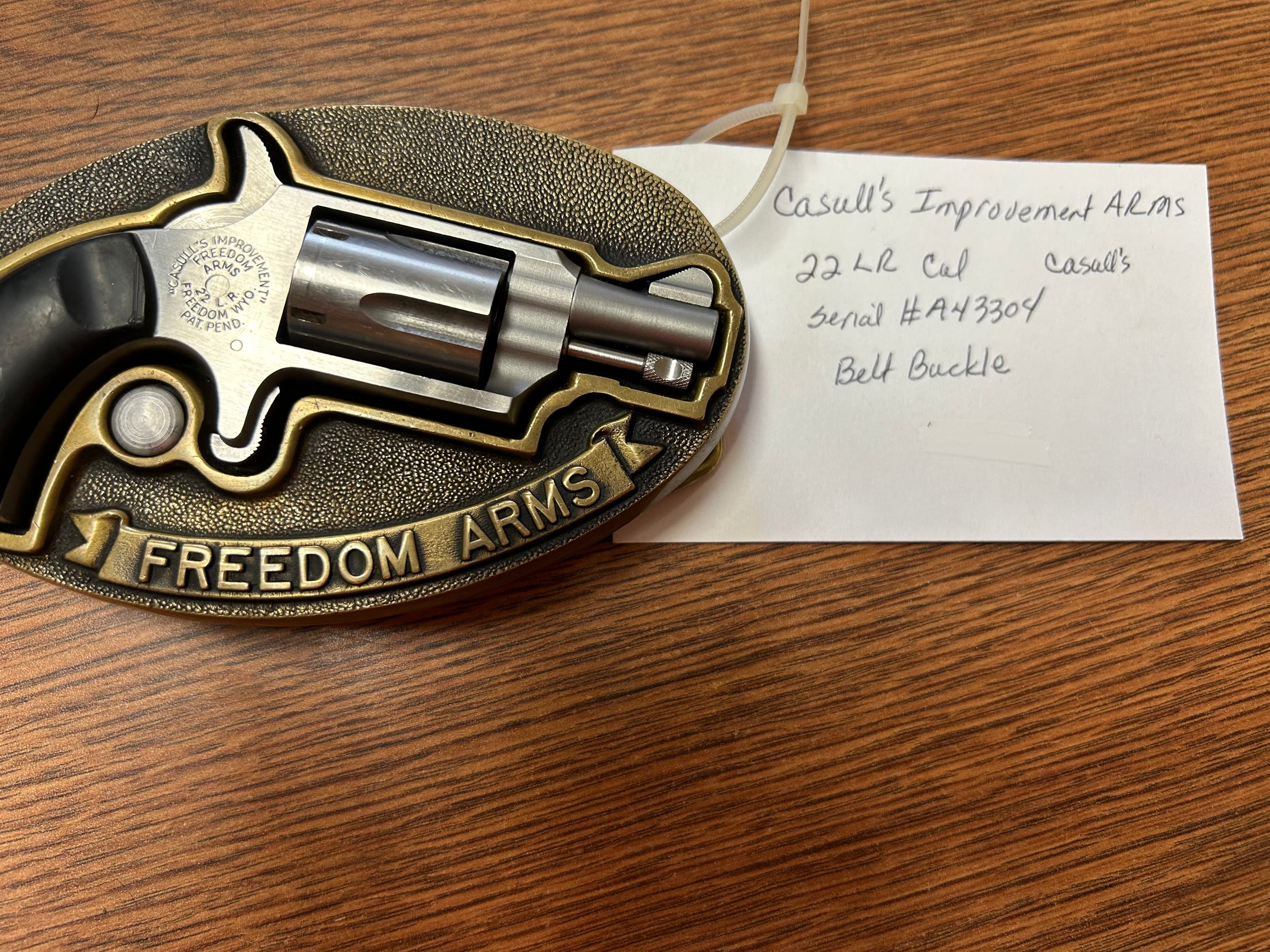 Freedom Arms belt buckle featuring a small .22 LR revolver mounted on a brass oval.