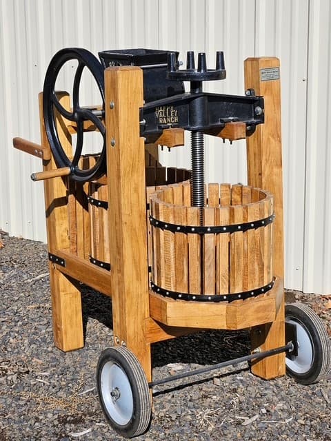 Double-barrel wooden cider press with a cast iron screw mechanism and large hand wheel.