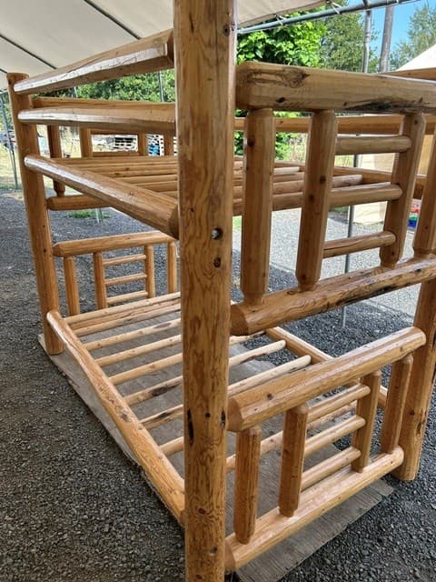 Rustic bunk bed frame made from thick, glossy logs, sitting outdoors on gravel.