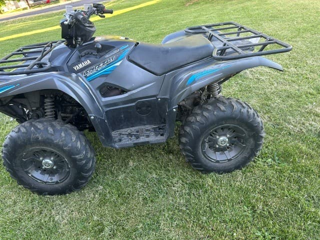 Charcoal gray Yamaha Grizzly ATV with blue accents parked on a green grassy lawn.