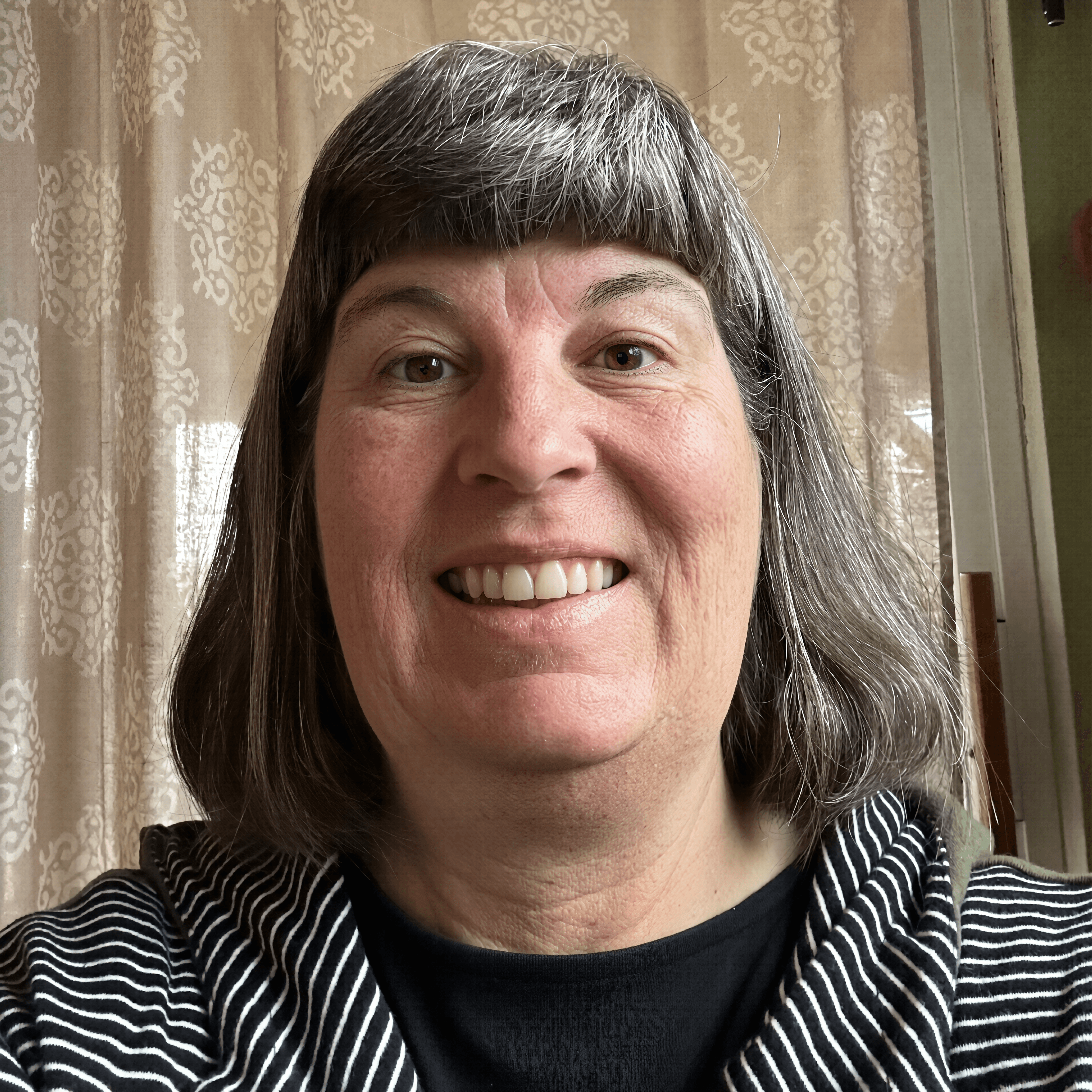 Smiling woman with salt-and-pepper hair and bangs, wearing a black and white striped top.