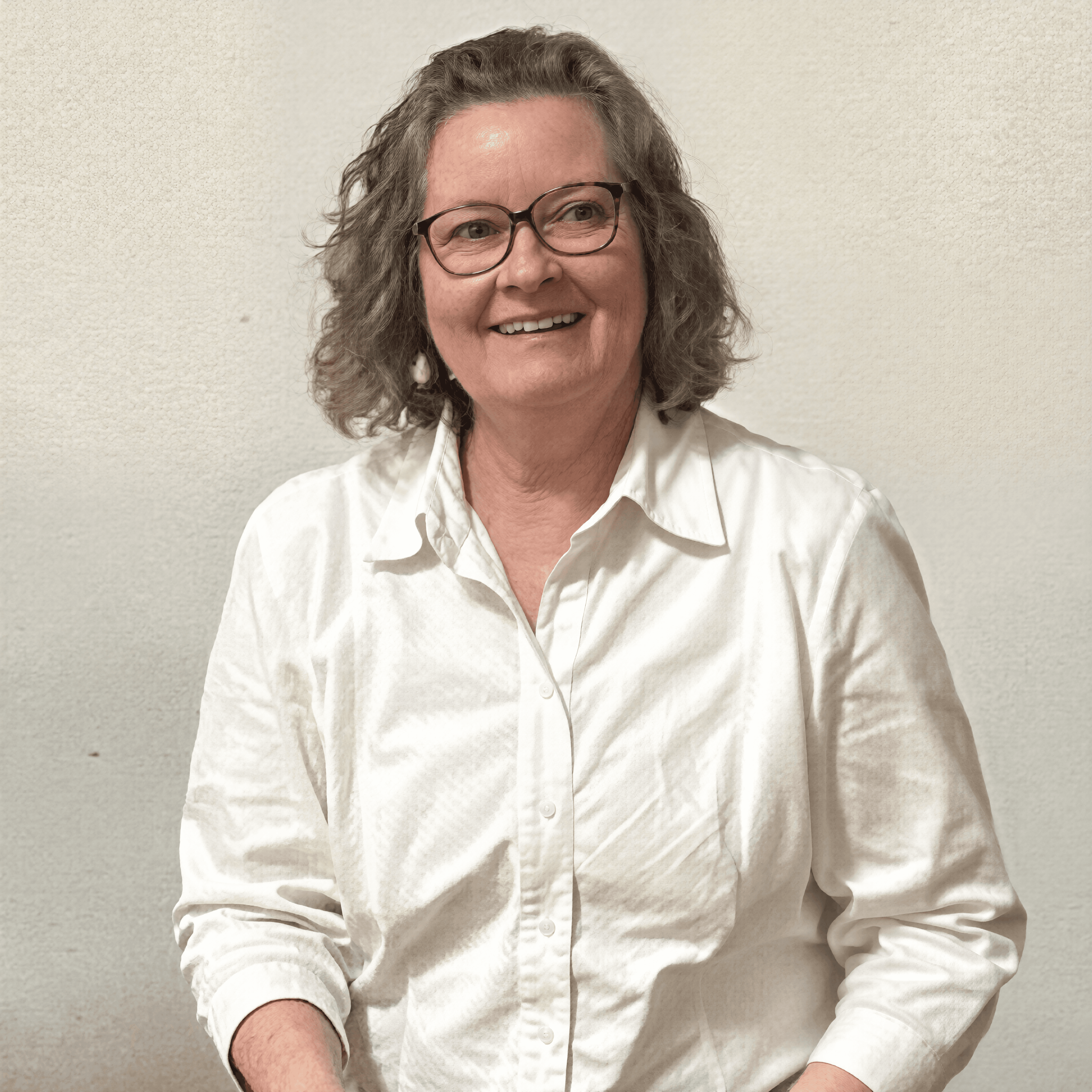 Smiling middle-aged woman with curly gray hair and glasses wearing a white button-down shirt.