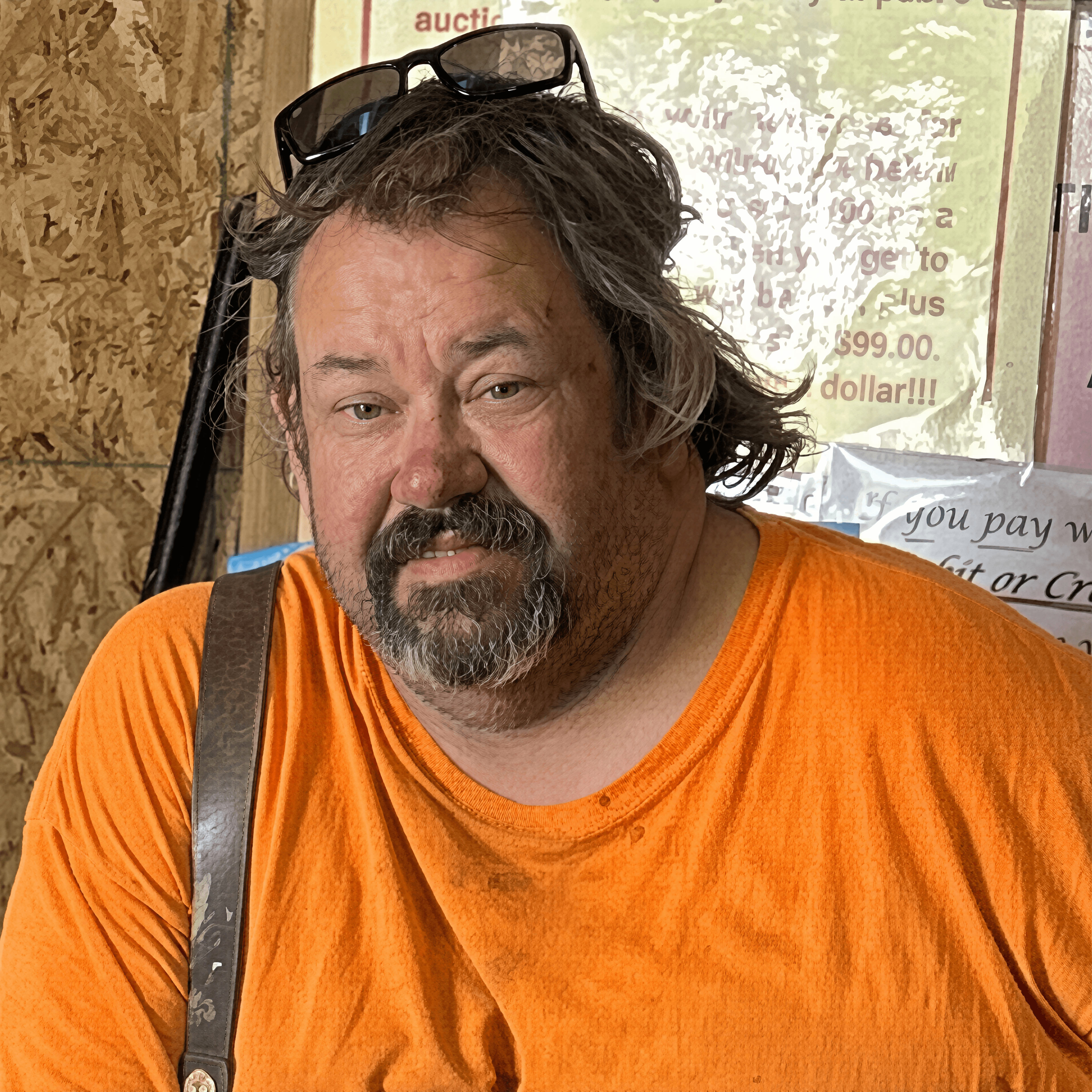 Man with messy hair and a goatee wearing a bright orange shirt and sunglasses.