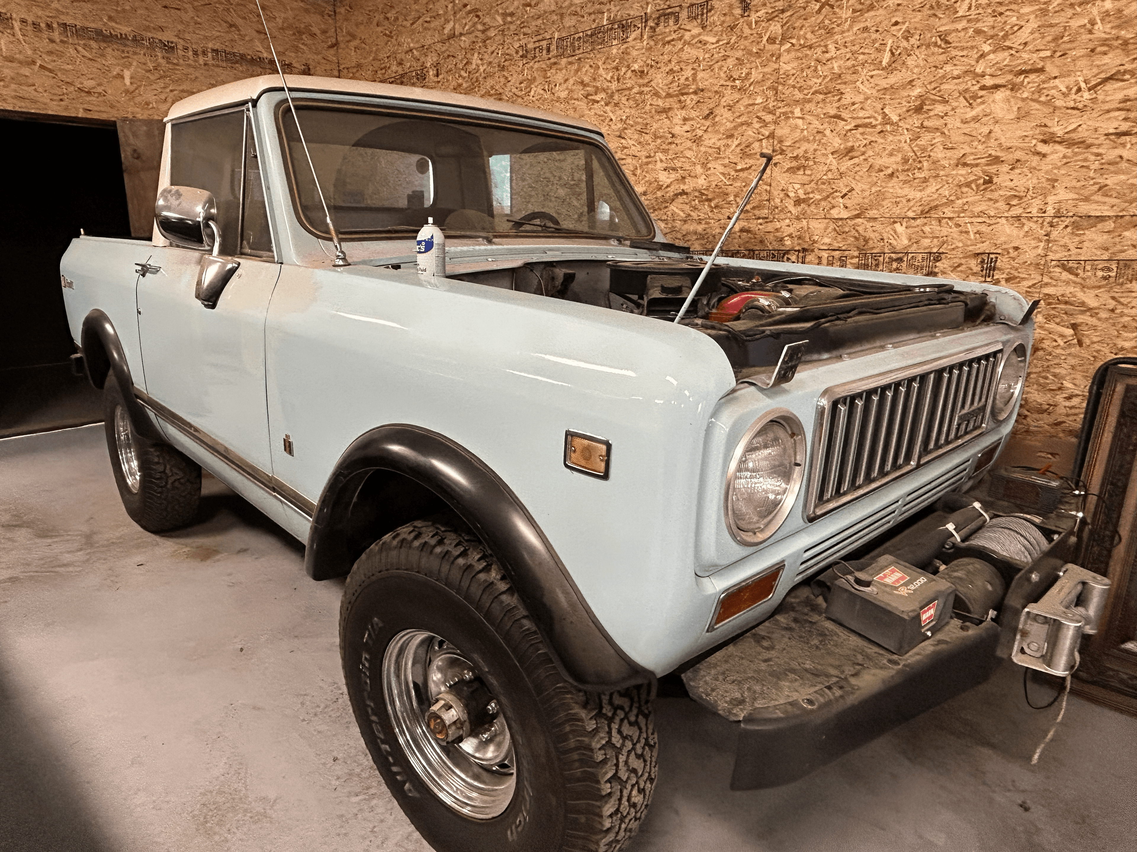 Light blue vintage International Harvester Scout truck with its hood open in a garage.