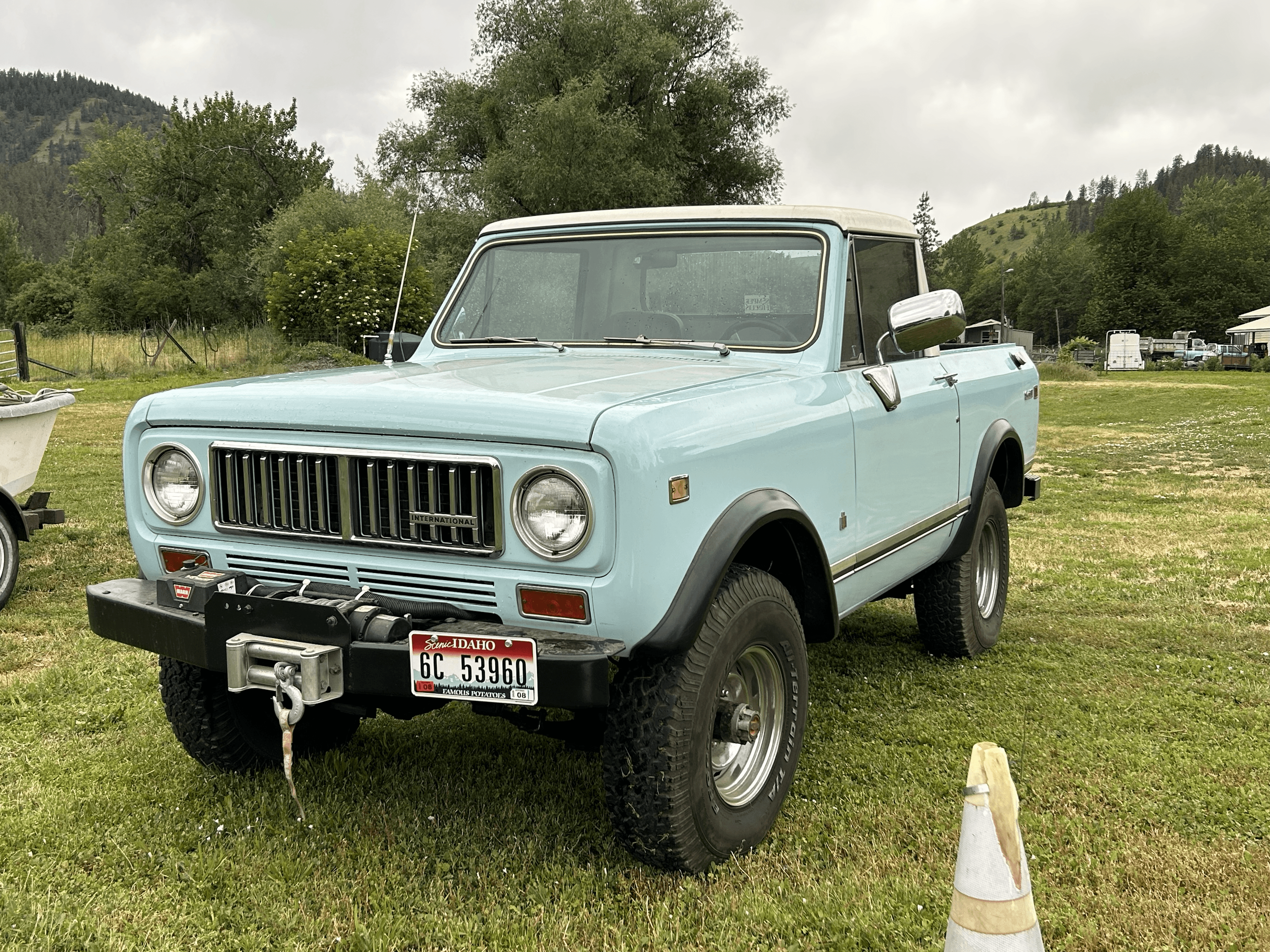 Light blue vintage International Scout truck with white roof parked on a grassy field.