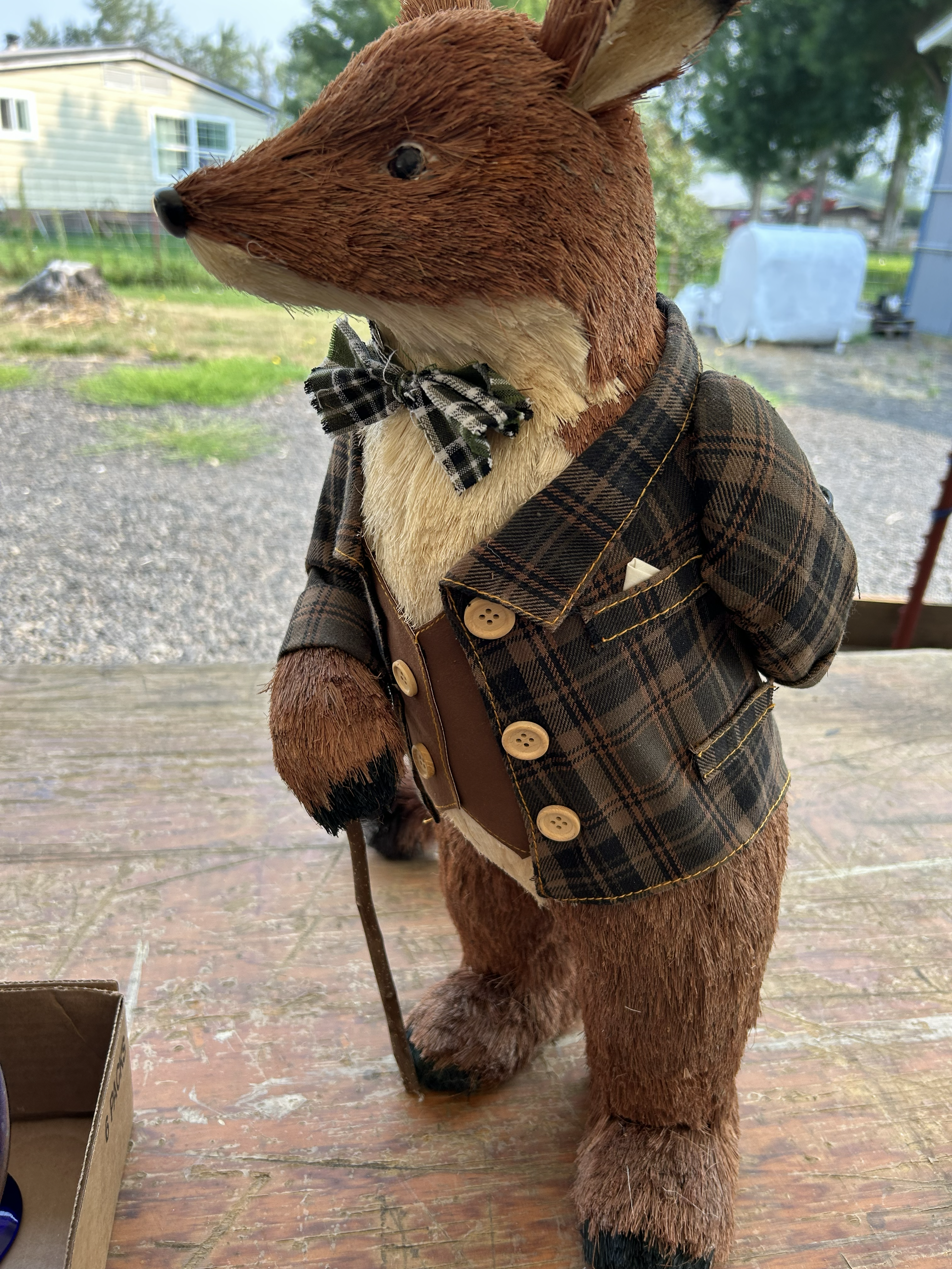 Decorative fox figurine wearing a brown plaid jacket and bow tie, holding a walking stick.
