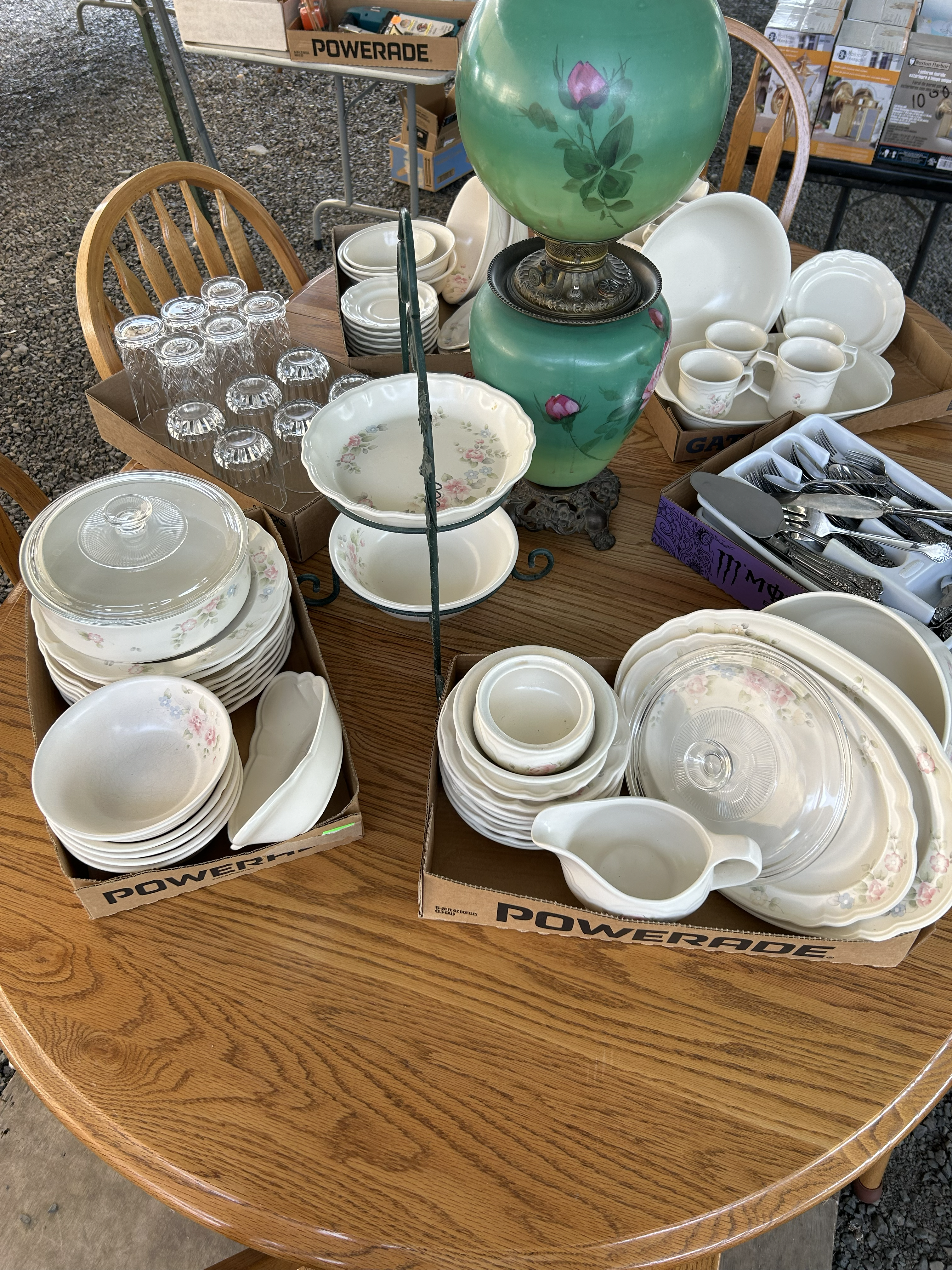 Vintage floral dinnerware, glassware, and a green lamp displayed on a wooden table for sale.