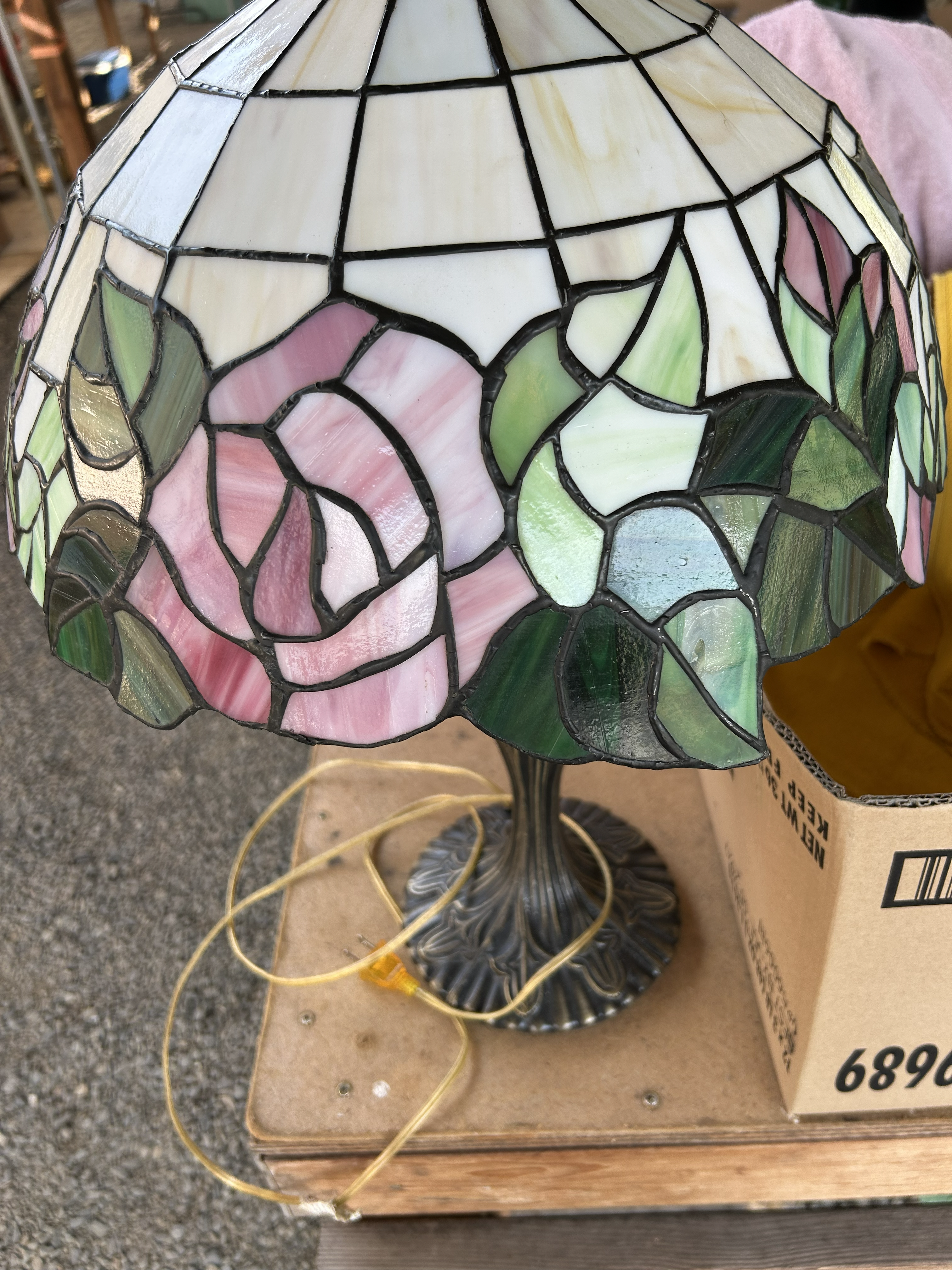 Stained glass table lamp with pink roses and green leaves on a fluted metal base.